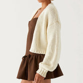 Person wearing a white knitted cardigan over a brown dress on a light gray background